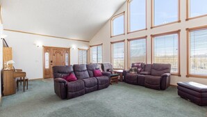 A spacious living room with a large sectional sofa, a small table, and a piano. - Grand View Ranch | 500+ Acres, Hot Tub, Sleeps 25, Forest Access! (Tetonia)