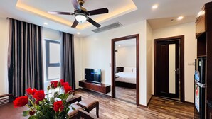 A hotel room with a ceiling fan, a flat-screen TV, a bed, a dining area with a table and chairs, and a refrigerator. - Hanoi Apartment  (Hanoi)