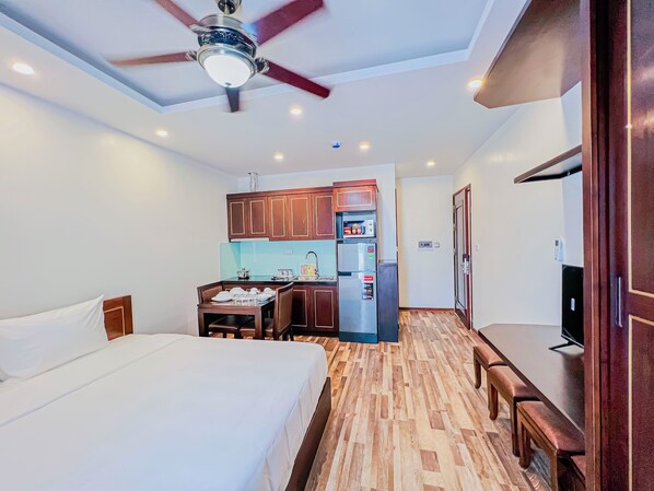 Habitación de hotel con cama, escritorio, kitchenette y ventilador de techo.