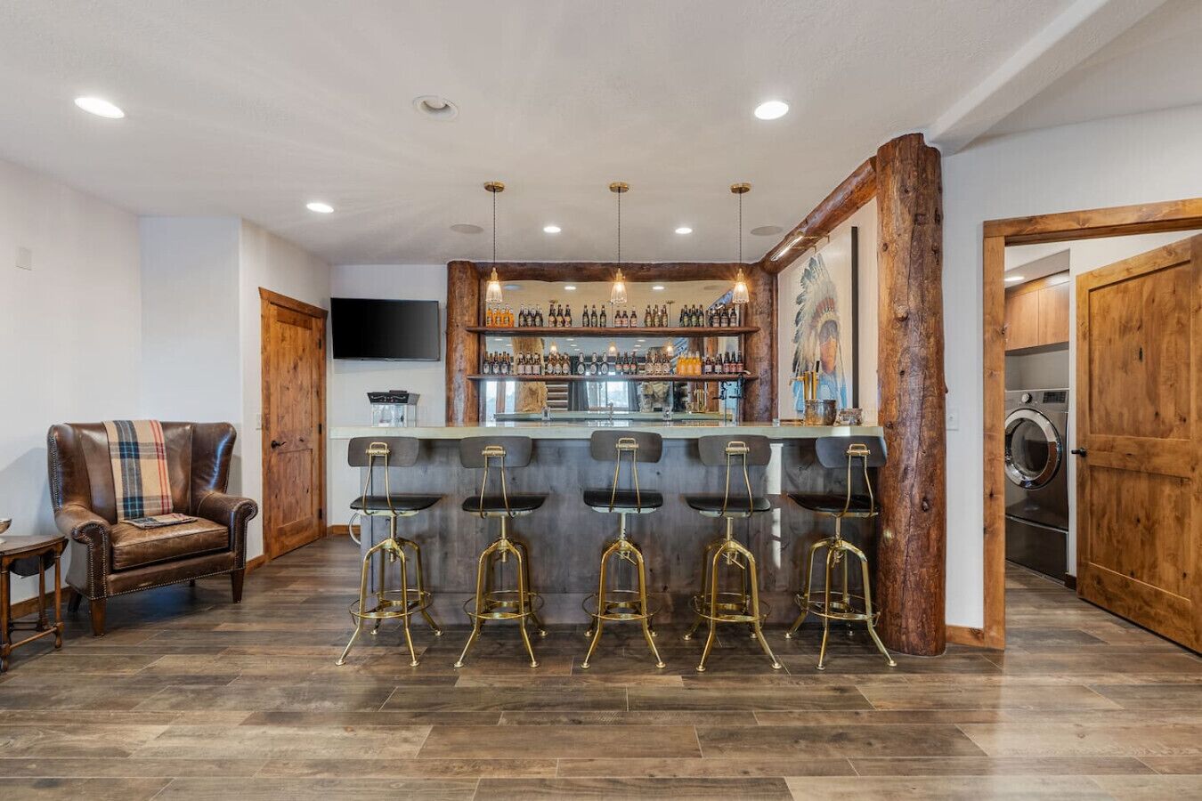 A bar area with a wooden bar counter, five stools, and a variety of bottles.