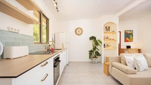 Een moderne keuken met een inbouwoven, een spoelbak en een aanrecht met een broodrooster. Er is een zithoek met een bank en een salontafel.