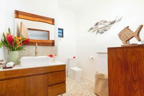 Ein Badezimmer mit einem Holzkosmetikschrank, einem weißen Waschbecken, einem Spiegel, einer Toilette und einer Duschkabine.