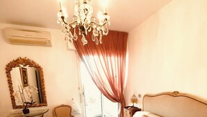 Ein Schlafzimmer mit einem großen Bett, einer Kristallleuchter, einem Spiegel und einem Fenster mit Vorhängen.