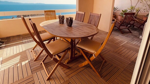 Ein runder Holztisch mit sechs Stühlen, einer Deckenleuchte und Blick auf das Meer.