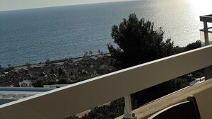 Ein Küstenblick mit blauem Himmel, der Sonne, die sich im Wasser spiegelt, und einer Stadt in der Ferne.