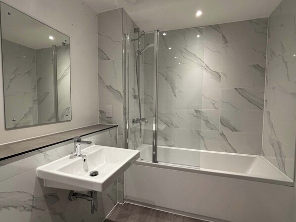 A modern bathroom with a glass-enclosed shower, a white sink, and marble-patterned walls.