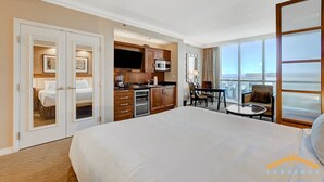 A hotel room with a large bed, a kitchenette, a dining area, and a view of the city.