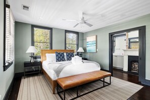 Un dormitorio moderno con una cama, dos mesitas de noche, un banco, un ventilador de techo y una chimenea.