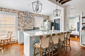 A kitchen with a large island, wooden chairs, and a brick wall. - Stylish 3BR | Sleeps 6 | Walk Everywhere (Charleston)