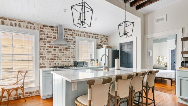 A kitchen with a large island, wooden chairs, and a brick wall.
