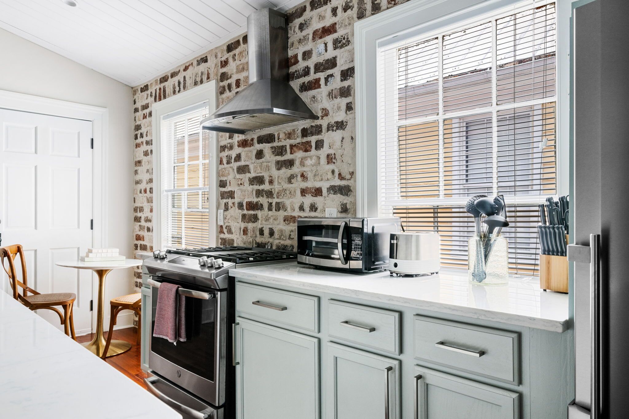 A kitchen with a brick wall, a stove, a microwave, and a window with blinds.