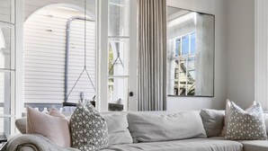 A modern living room with a sofa, a coffee table, and a view of a building outside. - Downtown|3 Beds|Luxury Rental (Charleston)