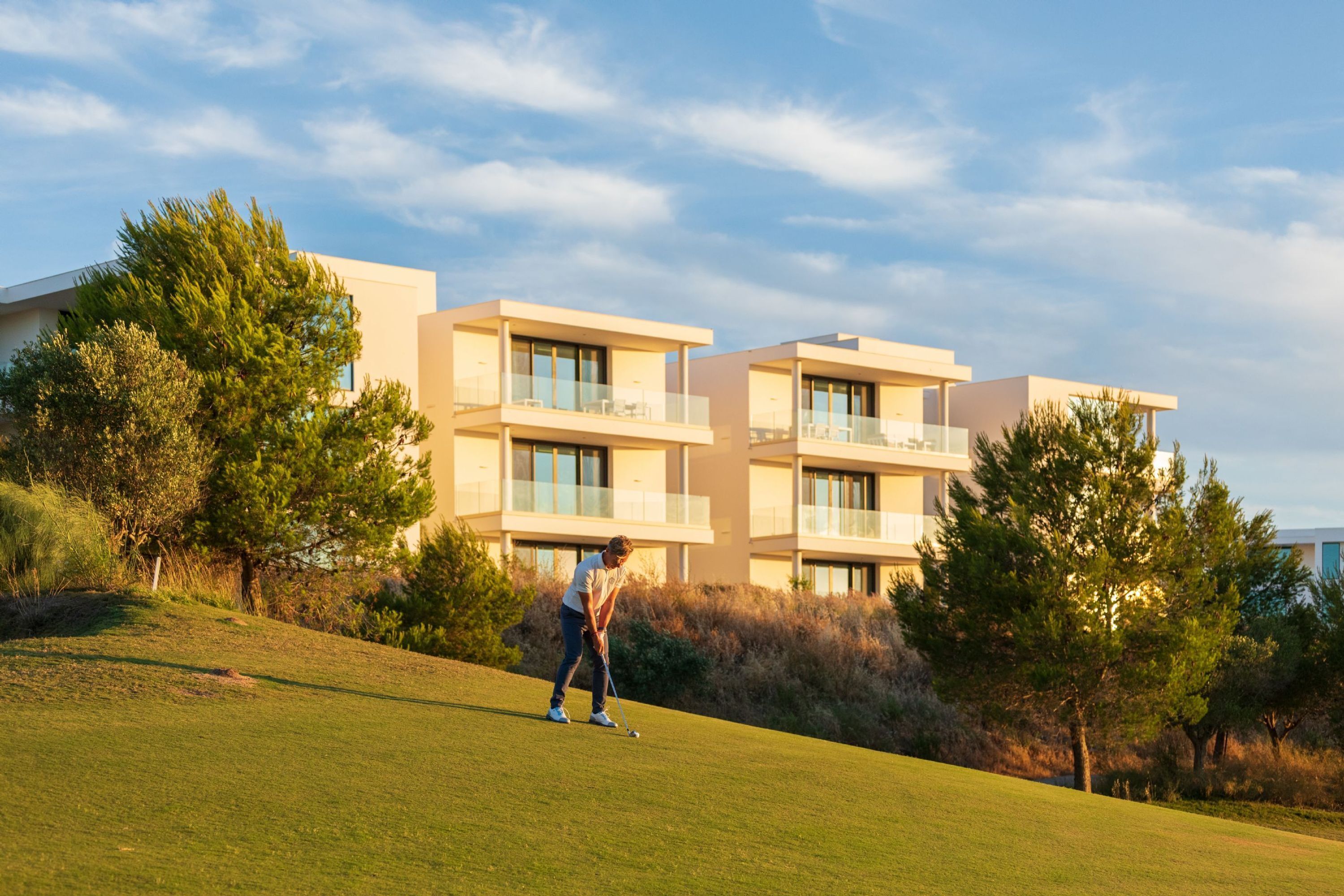 A modern building with multiple balconies and large windows, surrounded by trees and grass.