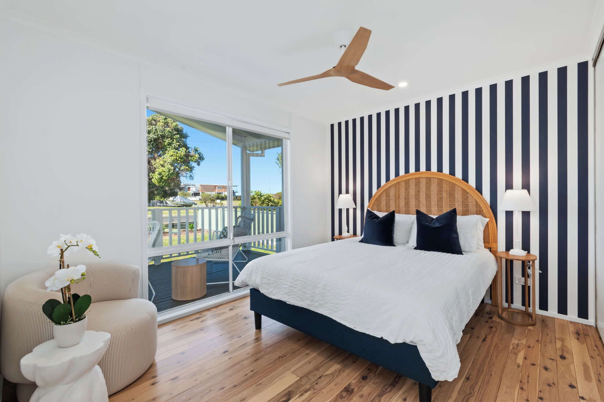 A bedroom with a large bed, a ceiling fan, a view through a sliding glass door, and a striped wall.