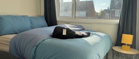 A bedroom with a bed, a bedside table with a lamp, and a window with curtains.
