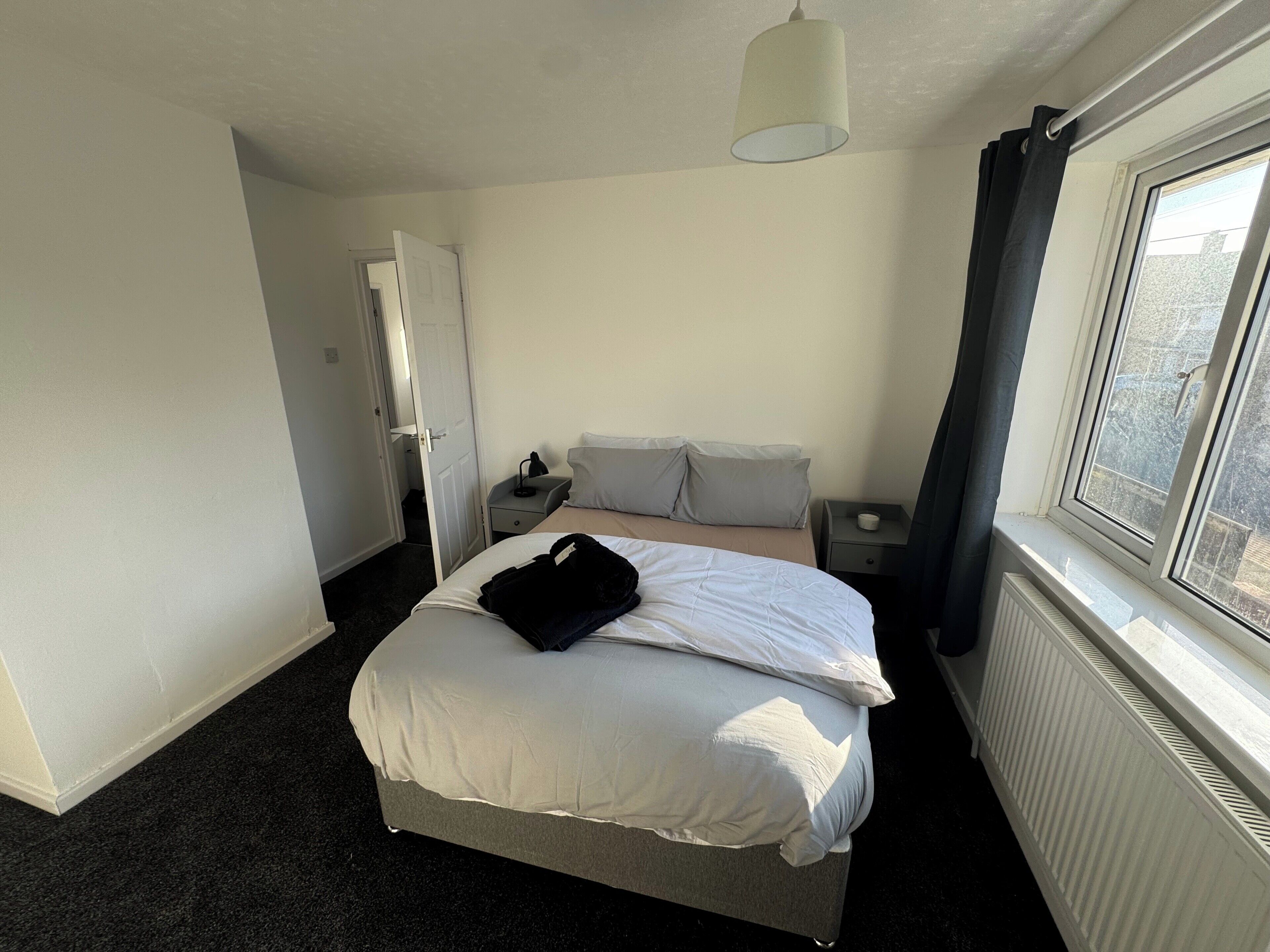 Hotellihuone, jossa on sänky, yöpöytä, lamppu ja ikkuna, josta on näkymä.