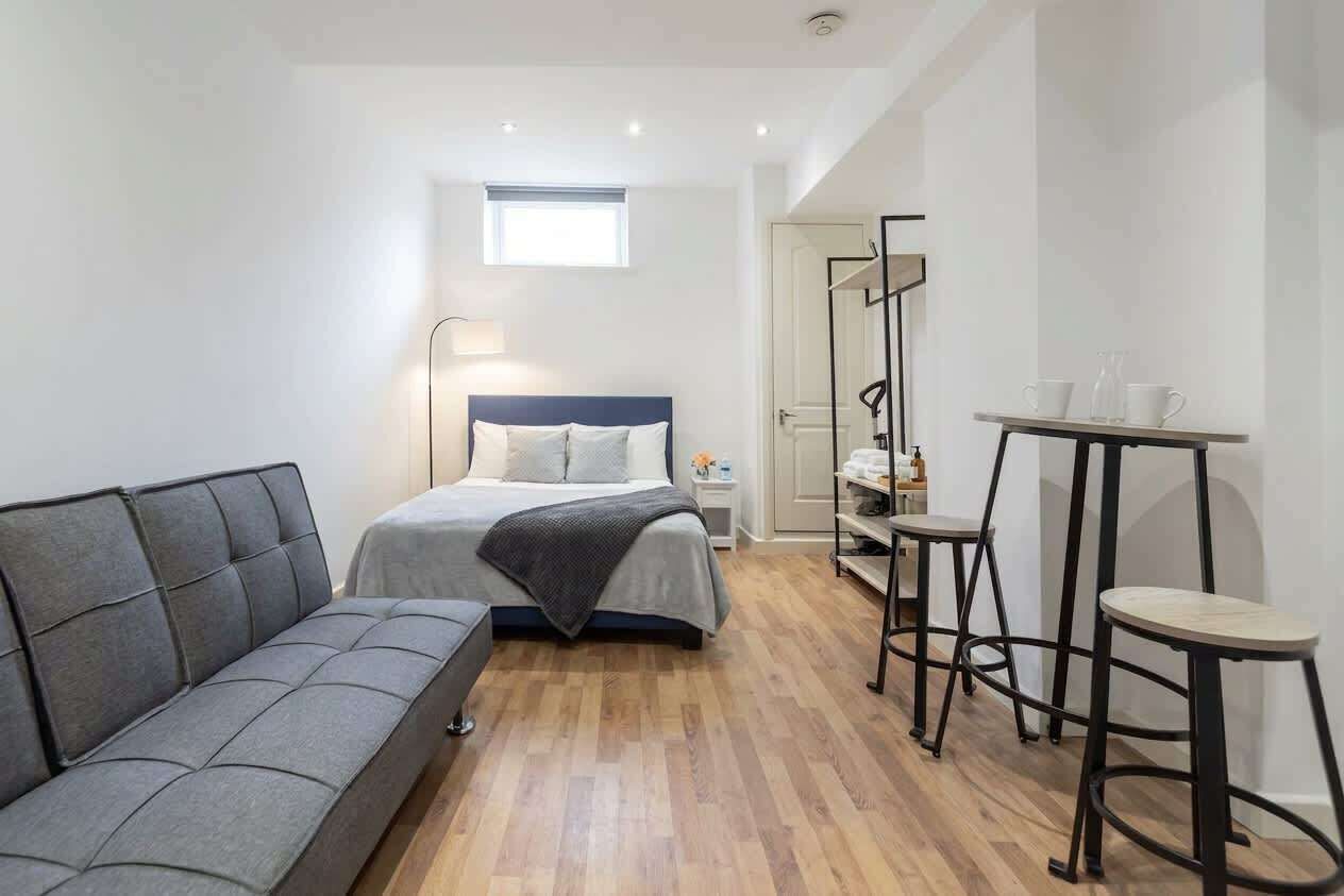 A compact bedroom with a bed, a sofa, a small table, and a mirror.
