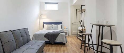 Un dormitorio compacto con cama, sofá, una mesita y un espejo.