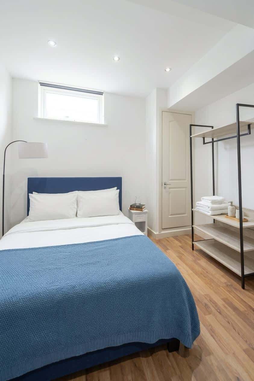 Une chambre à coucher comprenant un lit, une table de chevet, une commode, une fenêtre, une armoire et une étagère avec des serviettes.