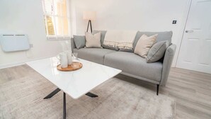 A modern living room with a white coffee table, grey sofa, and a lamp. - Stunning 1BR Cheltenham Suite Near Town Centre (Cheltenham)