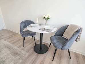 A dining area with a round table, two chairs, a vase with flowers, and a rug.
