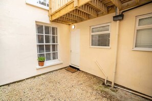 A small, enclosed outdoor area with a gravel floor, a potted plant, and a wooden staircase leading to an upper level.