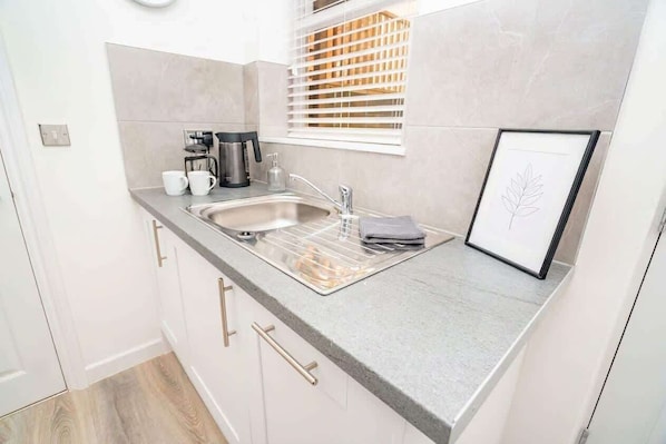 A compact kitchen with a sink, coffee maker, and a framed picture on the counter.