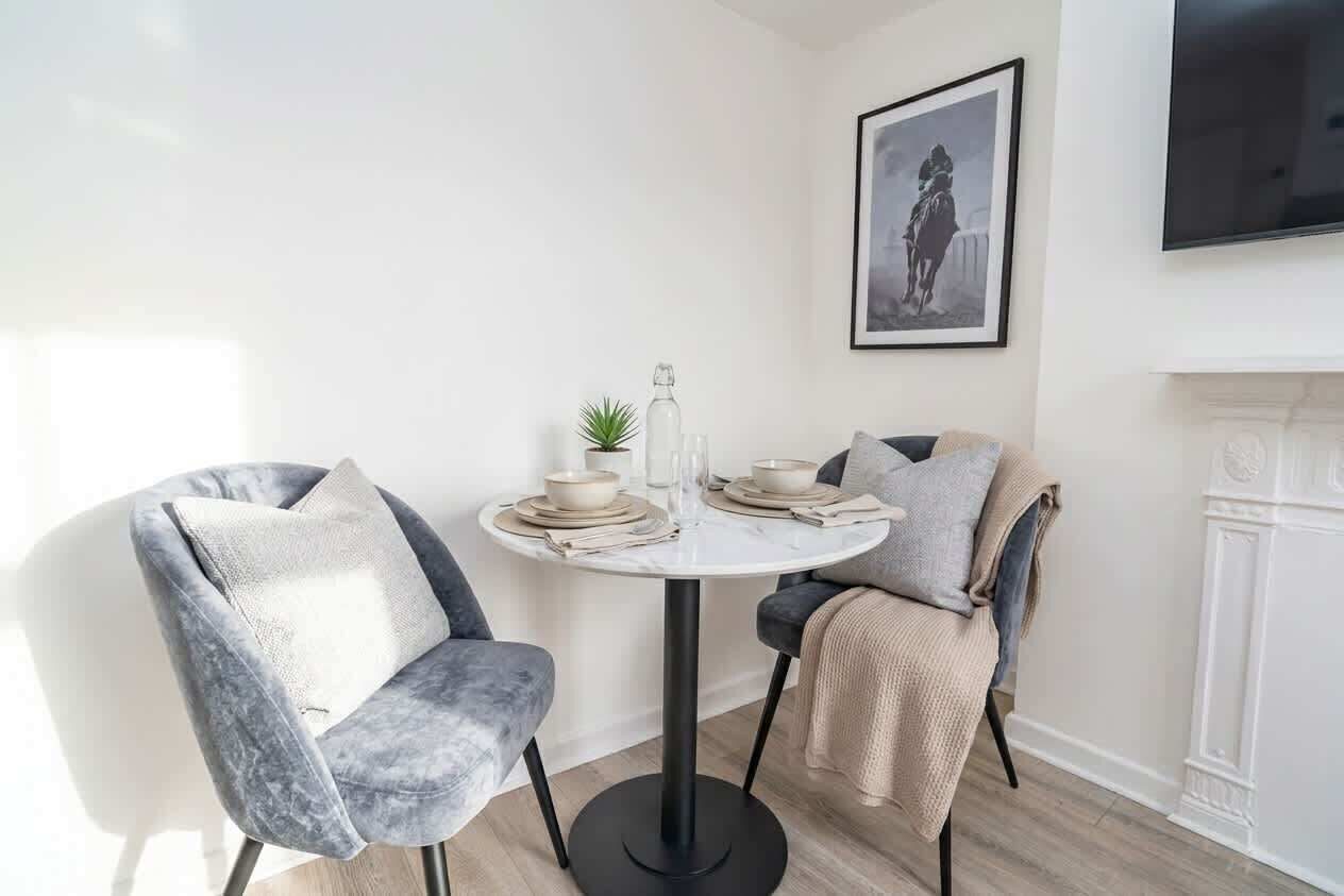 Een eetgedeelte met een ronde tafel, twee stoelen en een lijst met een afbeelding aan de muur.