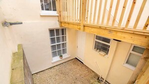 A small enclosed courtyard with a wooden balcony, two windows with shutters, and a gravel ground. - Stunning 1BR Cheltenham Suite Near Town Centre (Cheltenham)