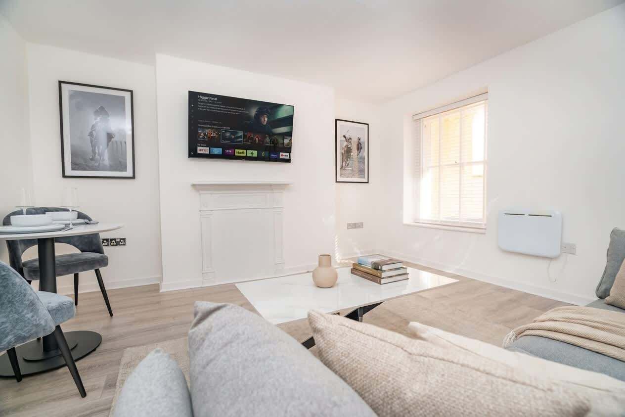 A modern living room with a fireplace, a flat-screen TV mounted above it, and a dining area with a table and chairs.