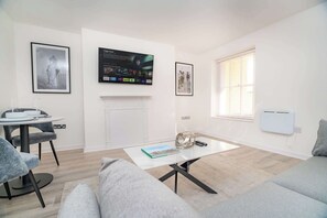 Un salon moderne doté d’une cheminée, d’un coin repas avec une table et des chaises, et d’un grand téléviseur à écran plat fixé au mur.