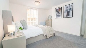 A bedroom with a bed, bedside table, lamp, and two framed pictures on the wall.