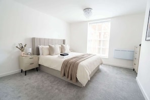 A bedroom with a bed, bedside tables, a nightstand, a window, and a radiator.