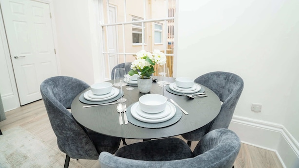A dining area with a round table set for four, surrounded by grey upholstered chairs.