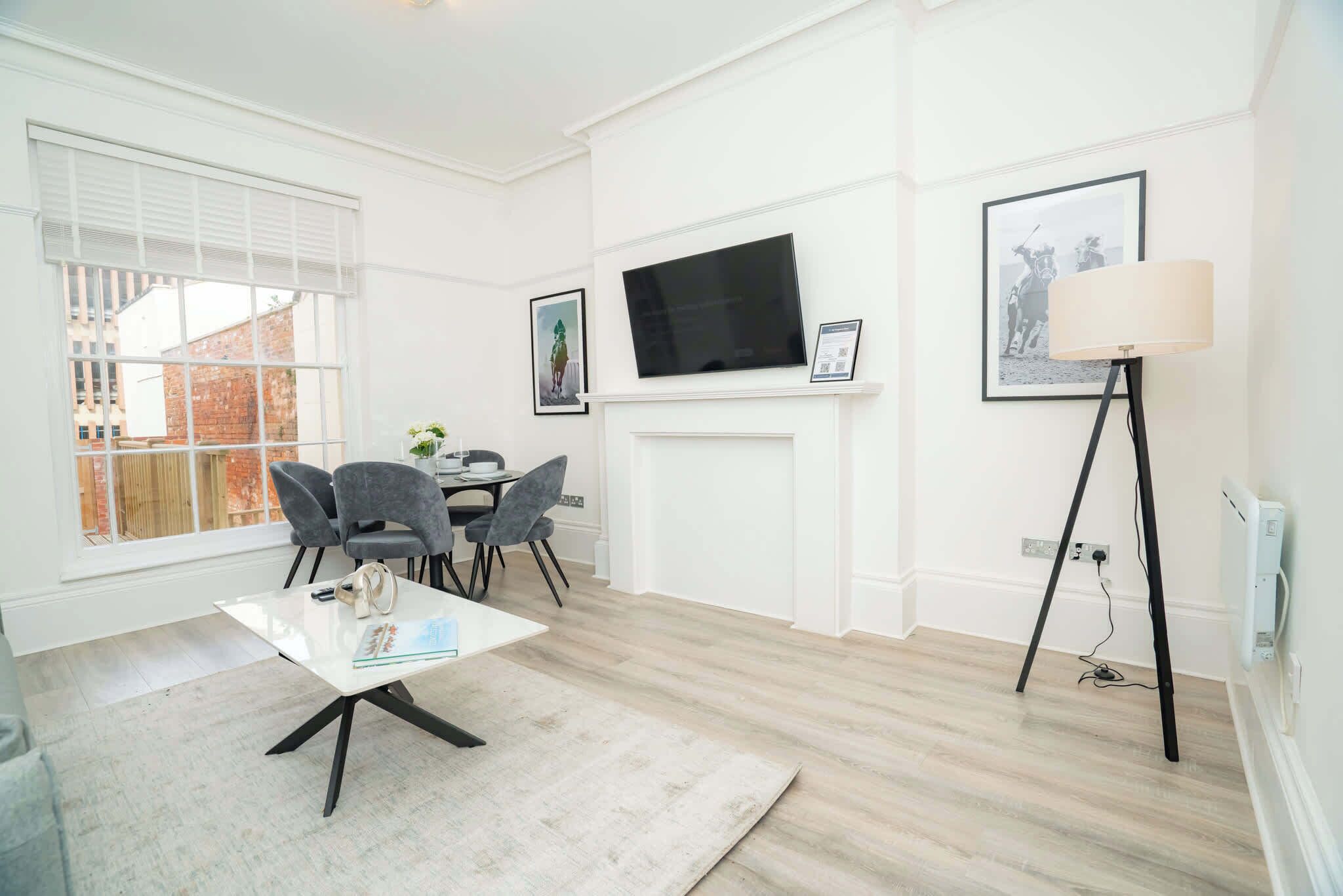 Un salon moderne avec une cheminée blanche, un téléviseur à écran plat fixé au-dessus, et un coin repas comprenant une table et des chaises.