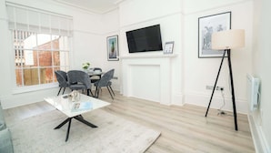 A modern living room with a white fireplace, a flat-screen TV mounted above it, and a dining area with a table and chairs.
