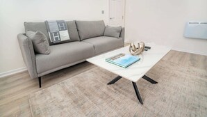 A living room with a grey sofa, a white coffee table, and a beige rug.