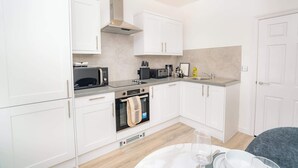 A modern kitchen with white cabinets, a stainless steel range hood, a microwave, a toaster, and a sink.