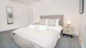 A bedroom with a large bed, two bedside tables with lamps, a mirror on the wall, and a door.