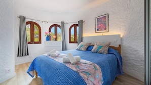 Ein Schlafzimmer mit einem großen Bett, zwei Vorhängen, einem Bild an der Wand und einer Vase mit Blumen auf einem Nachttisch.