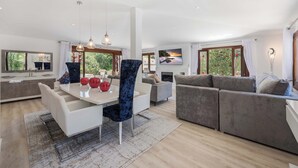 Ein modernes Wohnzimmer mit Essbereich, grauen Sofas und einem großen Fernseher.