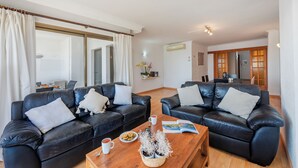 A living room with two black leather sofas, a wooden coffee table, and a dining area in the background. - Nitas Apartment (Pollença)