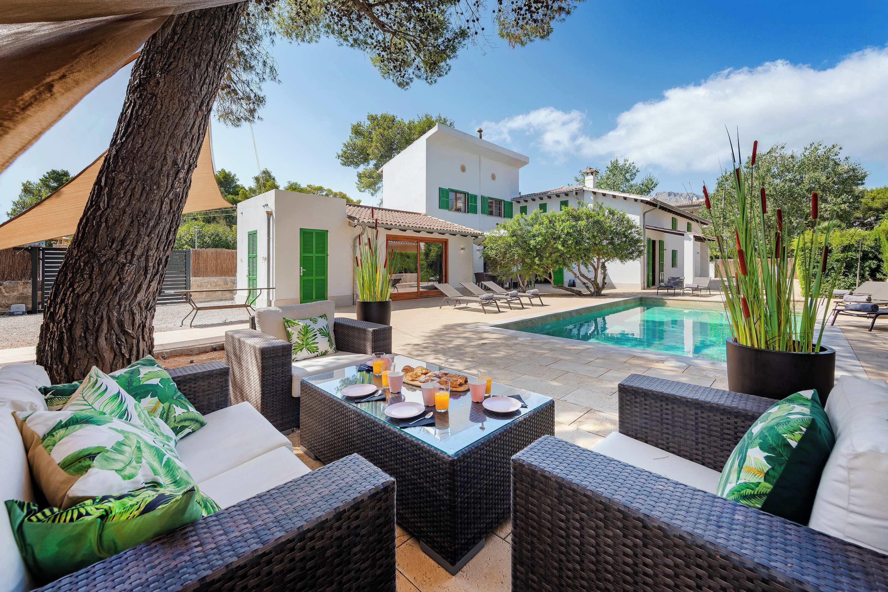 Un espace patio aménagé avec des meubles en osier, une table à manger pour deux personnes, et une piscine en arrière-plan.