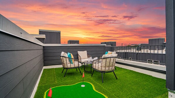A rooftop terrace with two wicker chairs, a small table, and a green artificial turf area.
