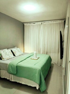 Ein Schlafzimmer mit einem Bett, einem Nachttisch mit Gegenständen darauf und einem an der Wand befestigten Fernseher.