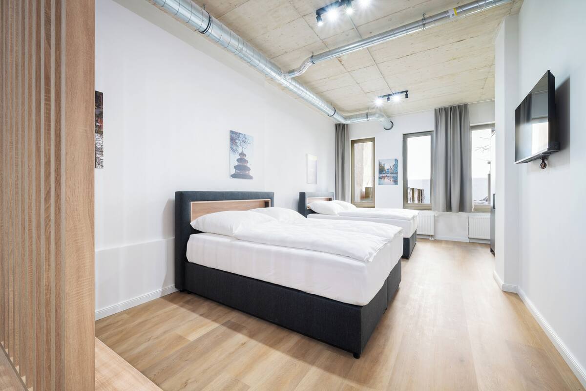 Ein modernes Hotelzimmer mit einem großen Bett, einem kleineren Bett, einem Fernseher und Blick auf die Stadt.