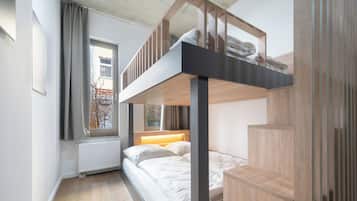 Dormitorio con literas, ventana, suelo de madera y radiador.