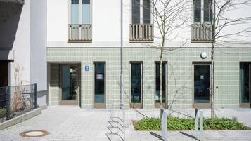 Un edificio moderno con fachada de baldosas, múltiples ventanas y un pequeño árbol en primer plano.