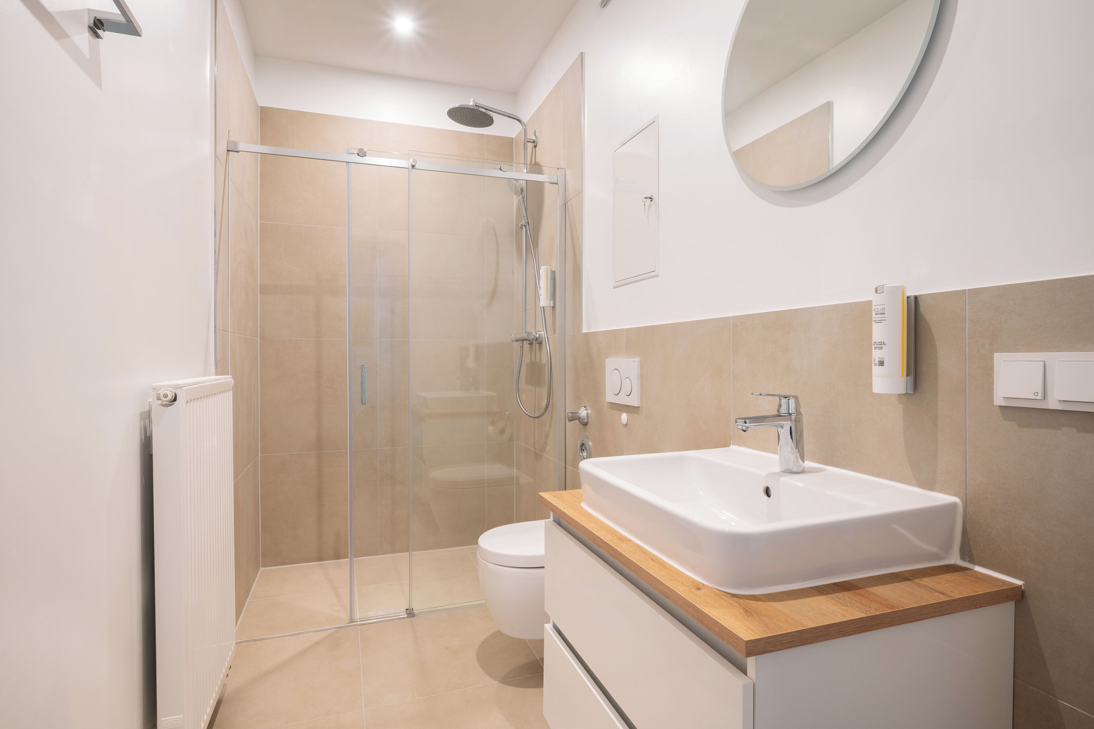 Une salle de bain moderne avec une douche à parois de verre, des toilettes blanches et un meuble-lavabo en bois avec un lavabo blanc.