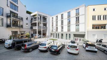 Un espace de stationnement où sont garées plusieurs voitures et un autobus, entouré de bâtiments modernes dotés de balcons et de grandes fenêtres.